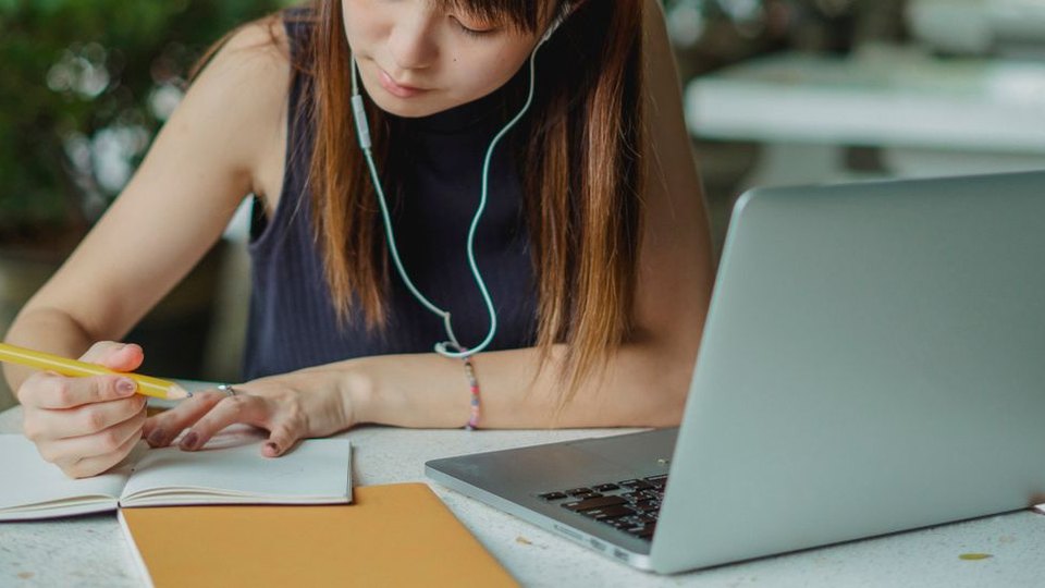 Student taking notes while learning with a laptop