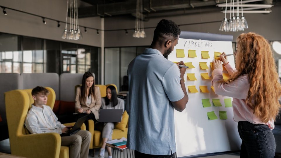 Two people organising sticky notes on a whiteboard