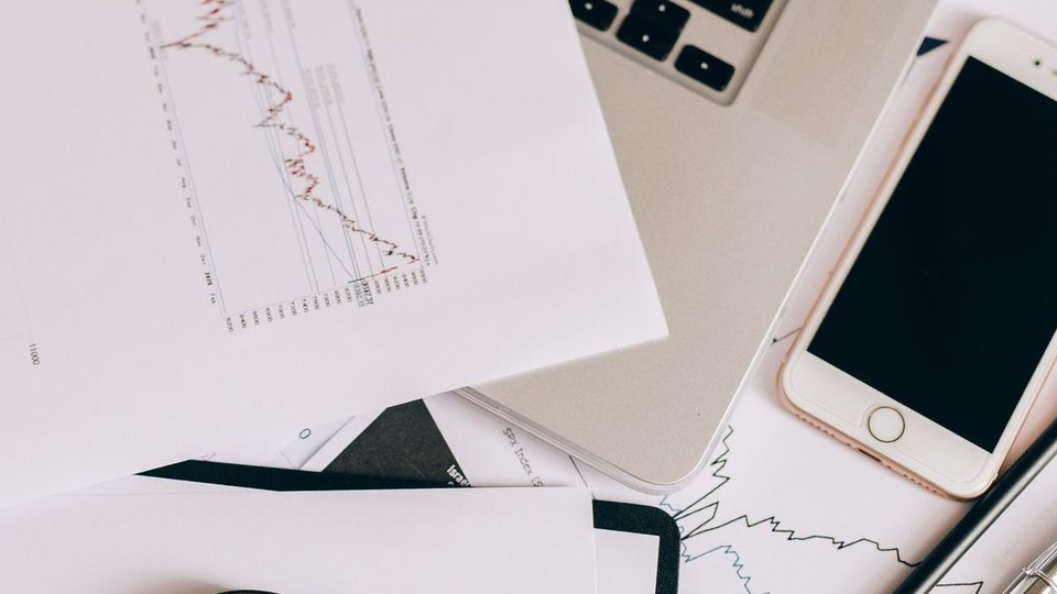 Printed reports beside a laptop and phone